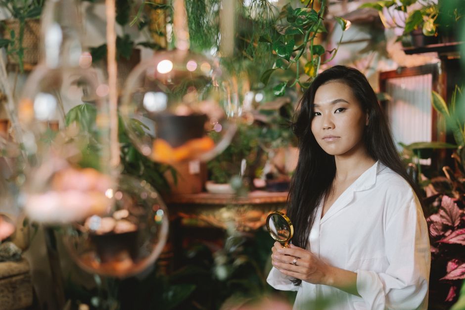 Female botanist examining plants with magnifying glass in a lush indoor setting.