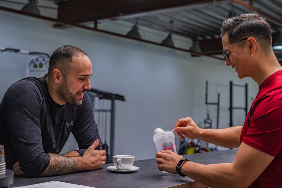 Side view of strong friends talking while preparing high protein smoothie after hard workout